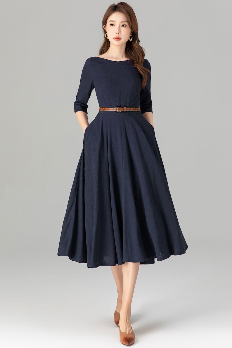 May include: A navy blue midi dress with a boat neckline and a brown belt. The dress has a full skirt and pockets on the sides.