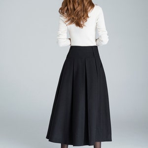 May include: A black midi skirt with a high waist and pleats. The skirt is made of a thick, woven fabric and falls to the ankles.