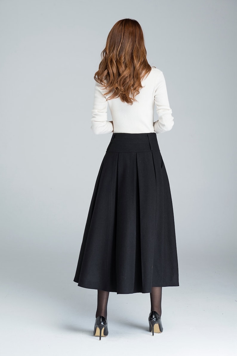 May include: A black midi skirt with a high waist and pleats. The skirt is made of a thick, woven fabric and falls to the ankles.