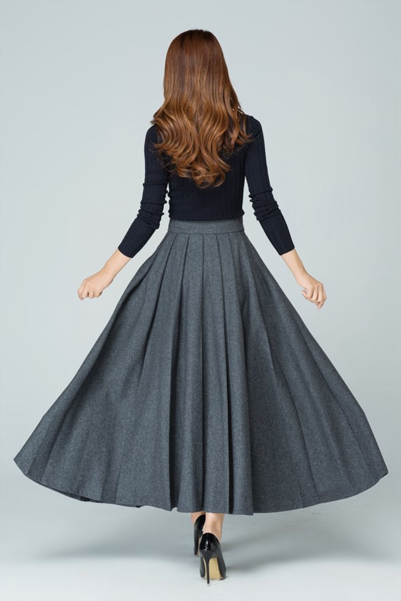 May include: A gray pleated maxi skirt with a high waistline. The skirt is made of a soft, flowing fabric and has a full, A-line silhouette.