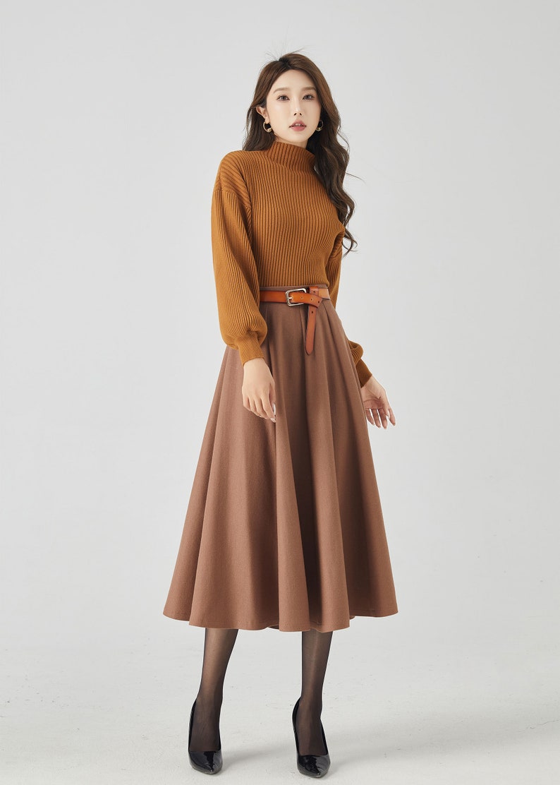 May include: A woman is wearing a brown turtleneck sweater with a brown skirt and a brown leather belt. She is wearing black tights and black heels.