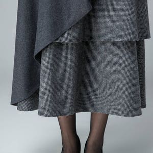 May include: A gray and white plaid skirt with a gray overlay. The skirt is knee-length and has a flowy silhouette.
