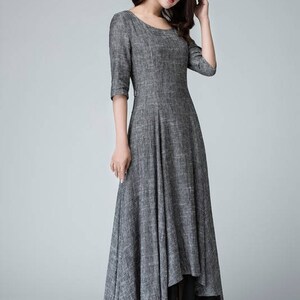 K&ouml;nnte beinhalten: Ein graues Leinenkleid mit einem hohen, niedrigen Saum. Das Kleid hat einen runden Ausschnitt und 3/4 &Auml;rmel. Das Kleid ist &uuml;ber einen schwarzen Chiffon-Slip gelegt.