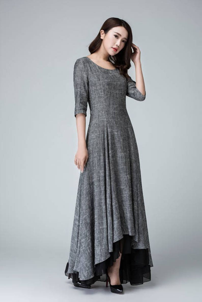 K&ouml;nnte beinhalten: Ein graues Leinenkleid mit einem hohen, niedrigen Saum. Das Kleid hat einen runden Ausschnitt und 3/4 &Auml;rmel. Das Kleid ist &uuml;ber einen schwarzen Chiffon-Slip gelegt.