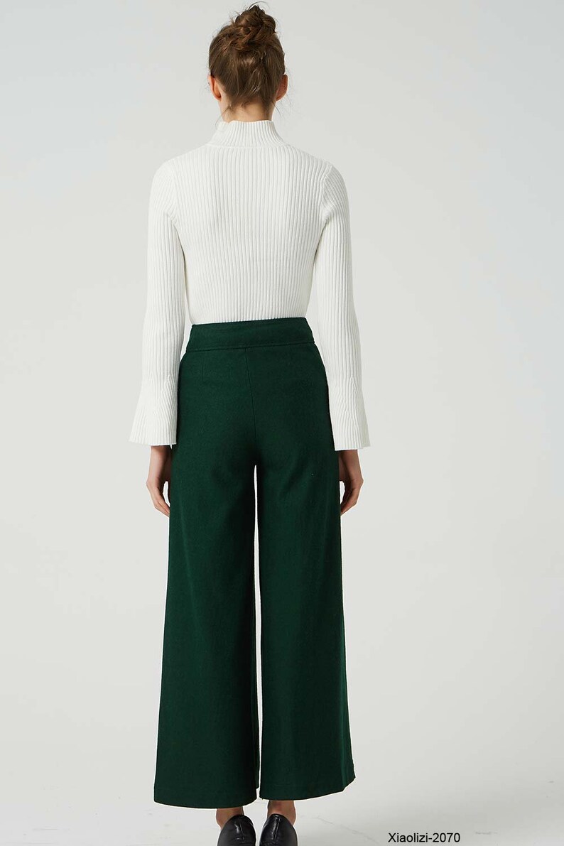May include: A woman wearing a white turtleneck sweater and dark green wide-leg trousers. The trousers have a high waist and a wide leg.