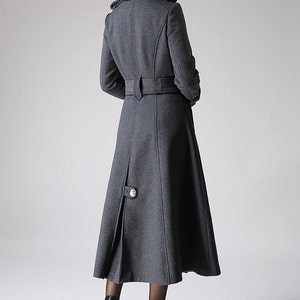 May include: A long, gray wool coat with a belted waist and a high collar. The coat has a single button closure at the bottom.