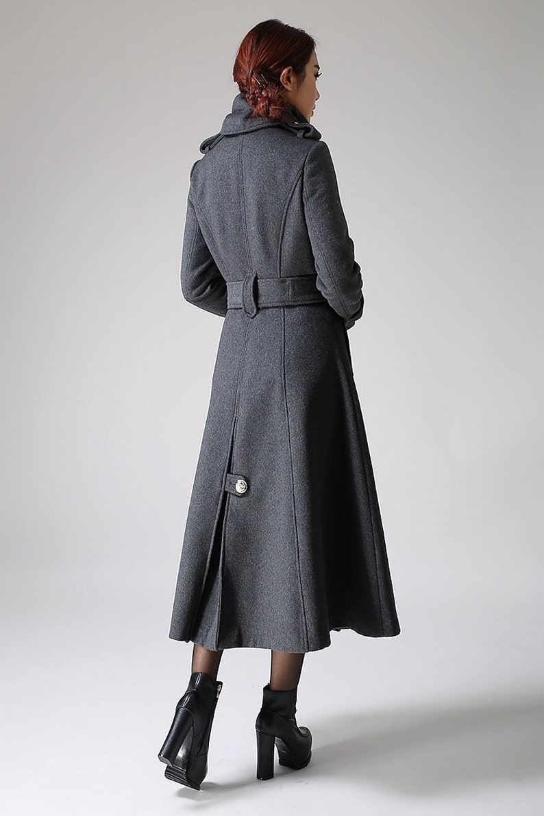 May include: A long, gray wool coat with a belted waist and a high collar. The coat has a single button closure at the bottom.