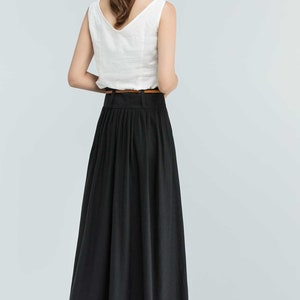 May include: A black maxi skirt with pleats and a brown belt. The skirt is made of a lightweight fabric and falls to the ankles.