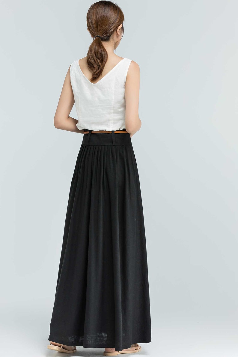 May include: A black maxi skirt with pleats and a brown belt. The skirt is made of a lightweight fabric and falls to the ankles.