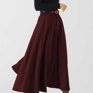 May include: A woman's outfit featuring a long-sleeved black top and a burgundy-colored, flowing skirt. The skirt is cinched at the waist with a brown belt. Black high-heeled shoes complete the ensemble.