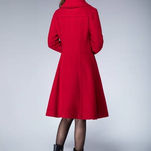 May include: A red wool coat with a flared skirt and a high collar. The coat is being worn by a person with brown hair and black boots.