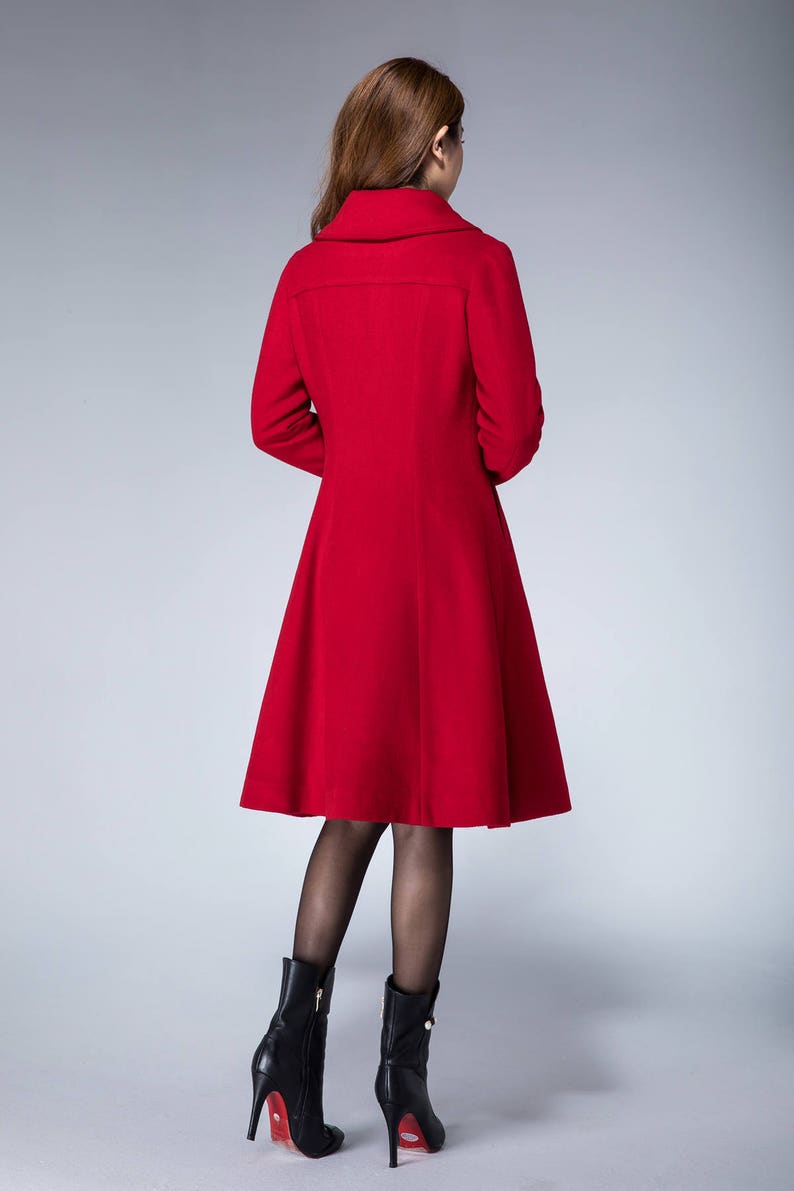 May include: A red wool coat with a flared skirt and a high collar. The coat is being worn by a person with brown hair and black boots.