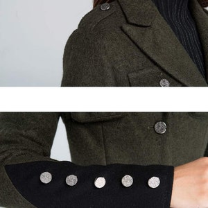 Puede incluir: Un abrigo de lana verde oscuro con ribetes negros en las mangas. El abrigo tiene botones plateados y un cuello.