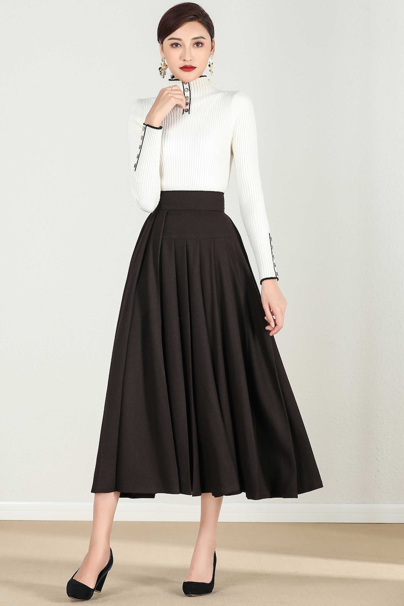May include: A brown midi skirt with a high waist and pleats. The skirt is made of a smooth fabric and has a flared silhouette.