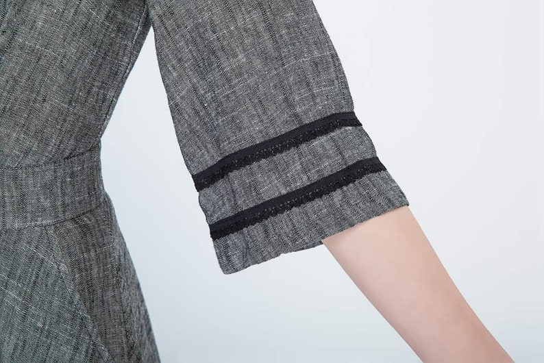 May include: Close-up of a gray linen dress with black lace trim on the sleeves.
