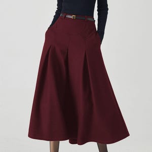 May include: A burgundy midi skirt with a high waist and pleats, paired with a navy blue long-sleeve top and a thin brown belt. The outfit is completed with black heels. The skirt's length is approximately 35 inches.