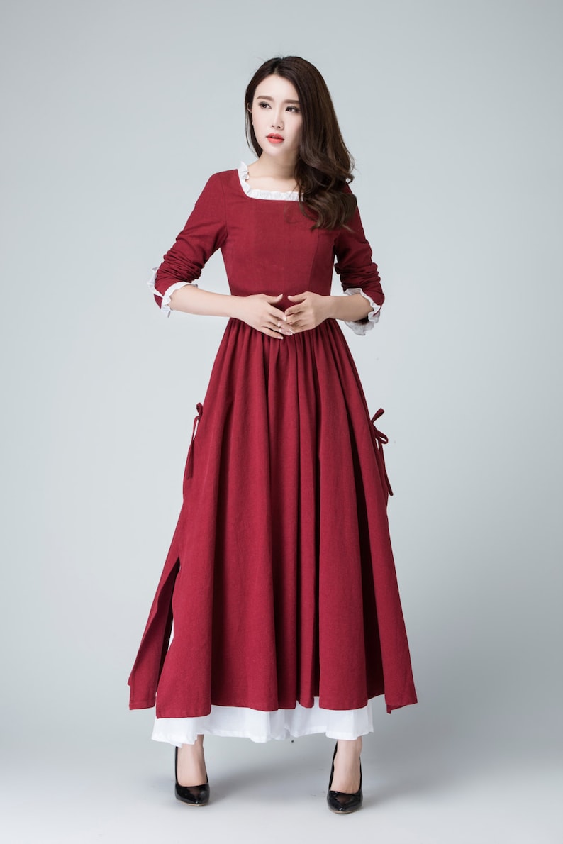 May include: A long, red dress with a white lace trim around the neckline and cuffs. The dress has a gathered skirt and a white underskirt.