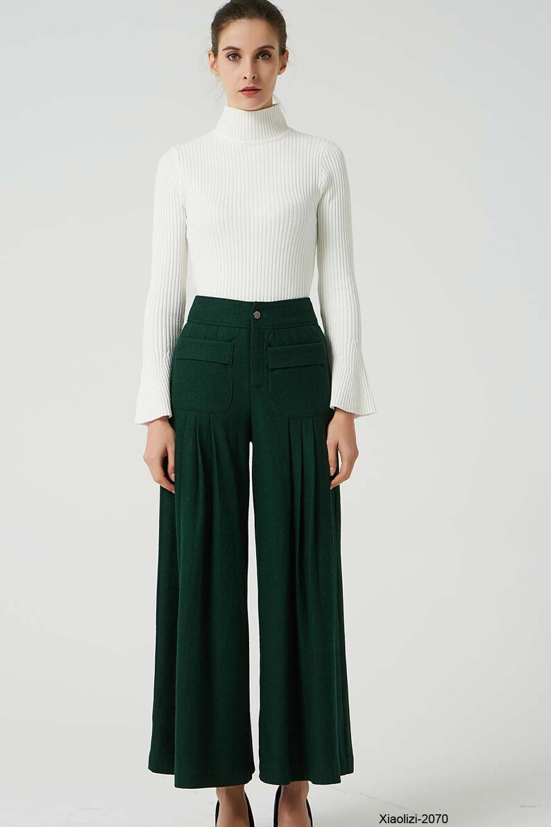 May include: A woman is wearing a white turtleneck sweater and dark green wide-leg trousers with pockets. The trousers have pleats and a button fastening.