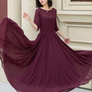May include: A burgundy maxi dress with a round neckline and 3/4 sleeves. The dress has a flowing skirt and is made of a lightweight fabric.