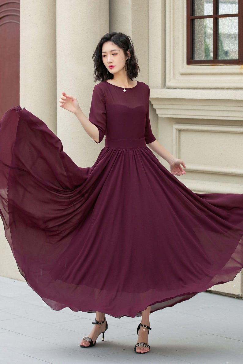 May include: A burgundy maxi dress with a round neckline and 3/4 sleeves. The dress has a flowing skirt and is made of a lightweight fabric.