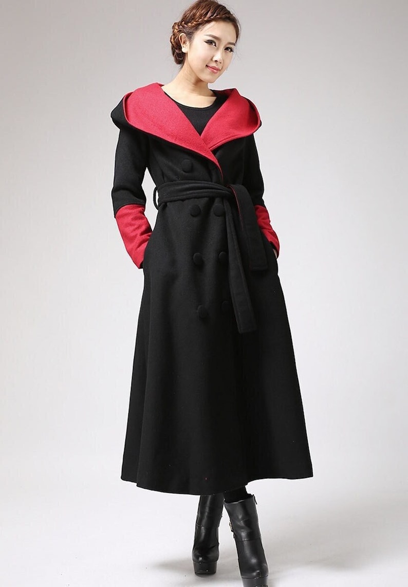 May include: A long black coat with a red hooded collar and a black belt. The coat has a double-breasted closure and two pockets.