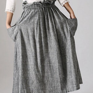 May include: A gray linen skirt with pockets and an elastic waistband. The skirt is paired with a white blouse with lace trim. The text "3-grey" is visible at the bottom of the image. The skirt is knee-length.