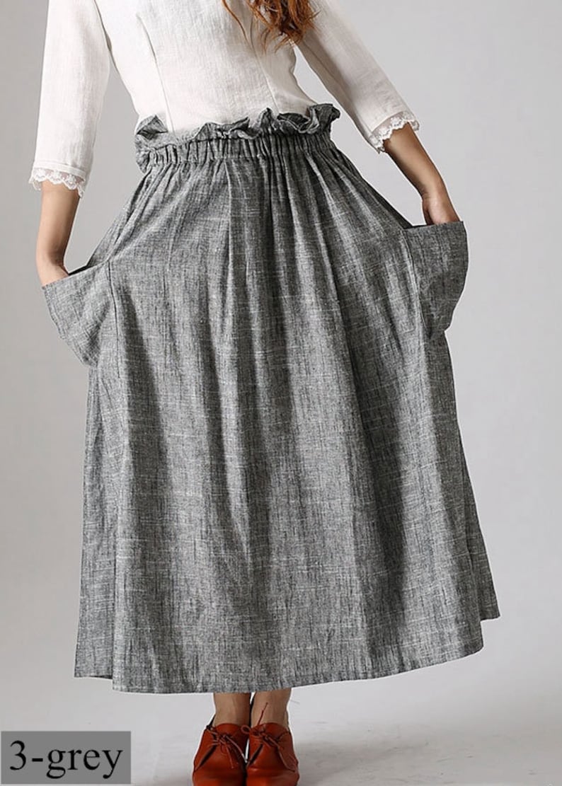 May include: A gray linen skirt with pockets and an elastic waistband. The skirt is paired with a white blouse with lace trim. The text "3-grey" is visible at the bottom of the image. The skirt is knee-length.