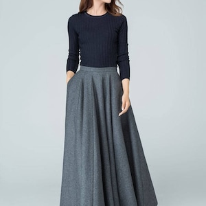 Op de afbeelding: Een vrouw draagt een zwarte longsleeve trui en een grijze maxi-rok. De rok heeft een wijde, vloeiende silhouet en is geplooid bij de taille.