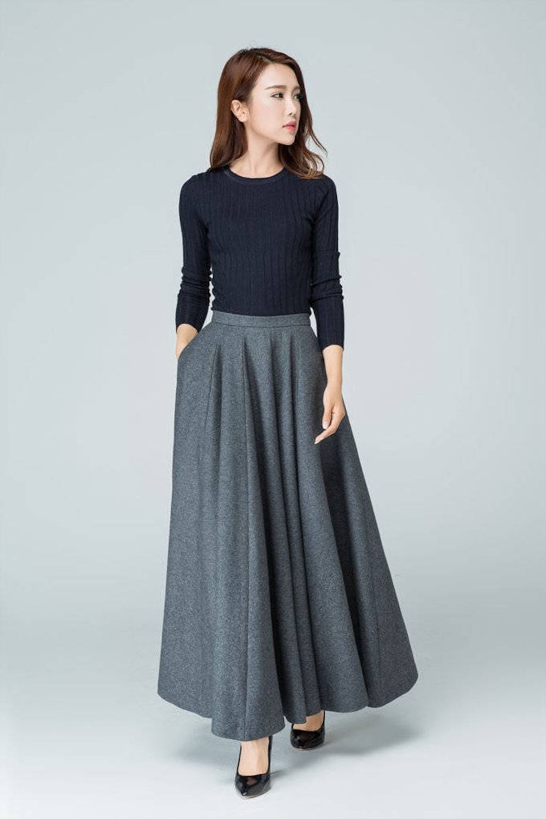 Op de afbeelding: Een vrouw draagt een zwarte longsleeve trui en een grijze maxi-rok. De rok heeft een wijde, vloeiende silhouet en is geplooid bij de taille.