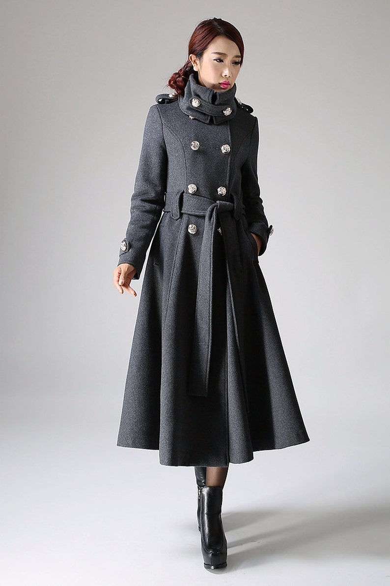 May include: A long, gray wool coat with a high collar, double-breasted closure, and a belt. The coat has a flared skirt and silver buttons.