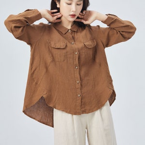 May include: A brown linen shirt with a collared neckline, long sleeves, and two flap pockets. The shirt has a curved hemline and is button-up.