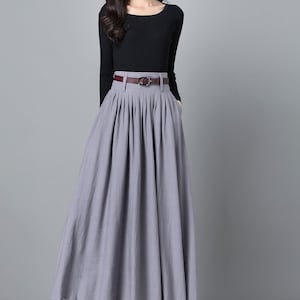 May include: A grey maxi skirt with a brown belt and pleats. The skirt is made of a soft, flowing fabric and has a high waist.