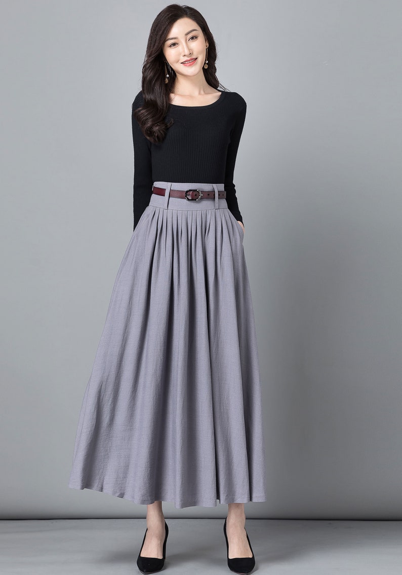 May include: A grey maxi skirt with a brown belt and pleats. The skirt is made of a soft, flowing fabric and has a high waist.