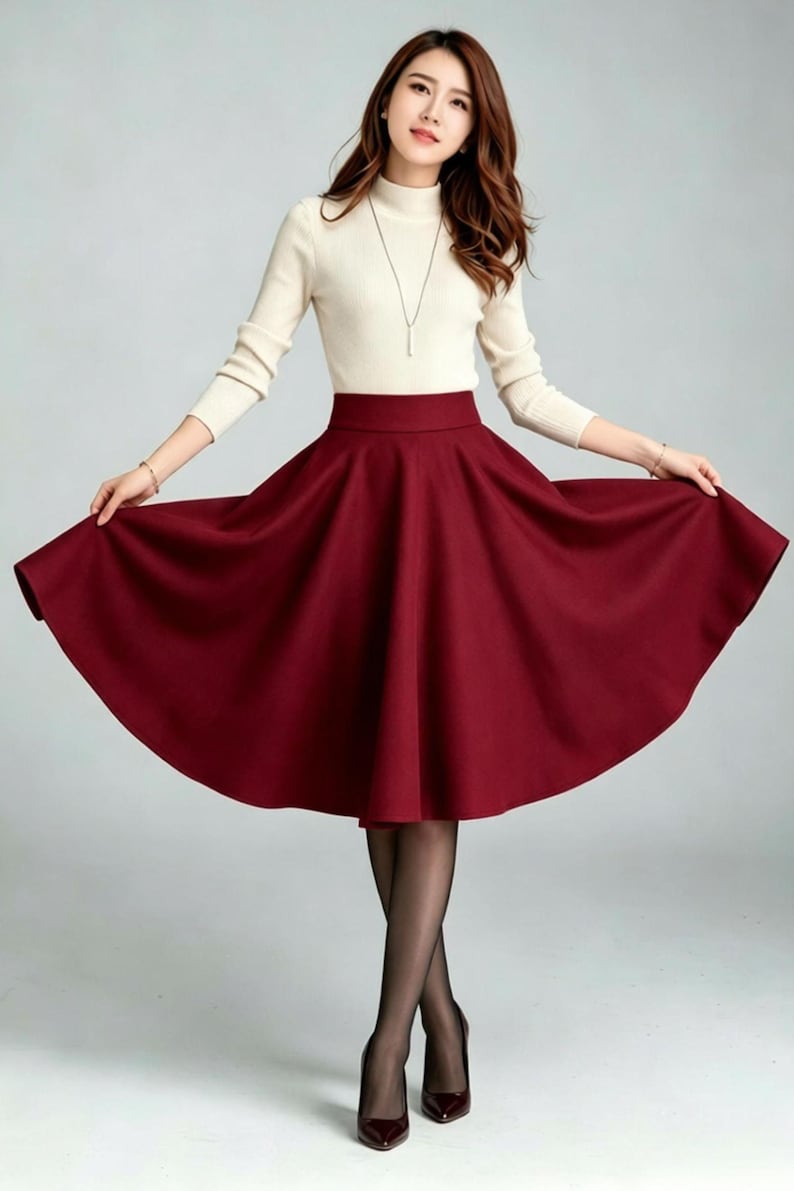 May include: A cream-colored long-sleeve mock neck top paired with a solid deep red high-waisted midi skirt. The skirt features a wide waistband and a full, flared silhouette that extends outward. The outfit is completed with sheer black tights.