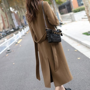 May include: A brown belted long coat with a black chain strap bag that says "CHANEL" on the side.