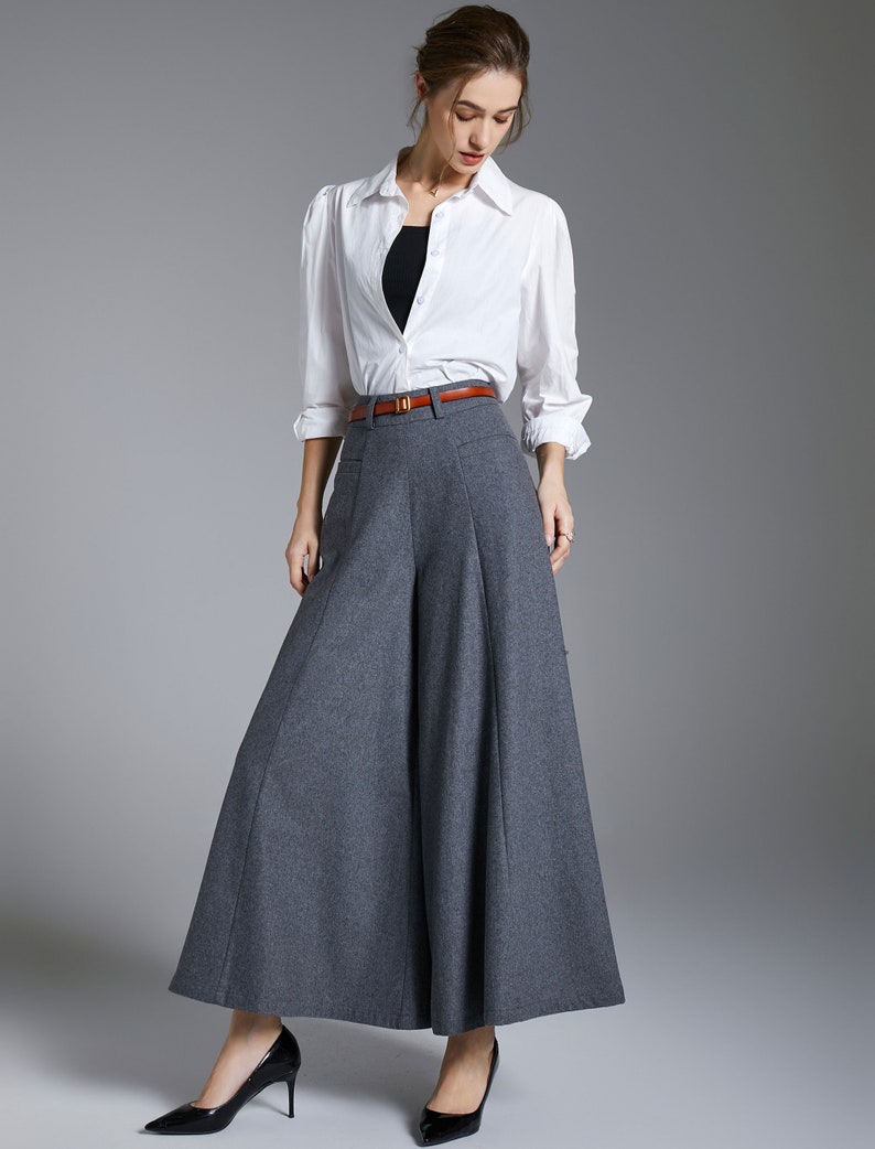 May include: A woman wearing a white button-down shirt with a brown belt and gray wide-leg pants.