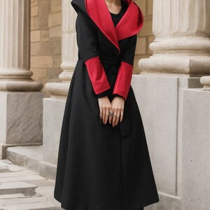 May include: A black hooded coat with red trim on the hood and sleeves. The coat has a tie belt and a long, flowing skirt.