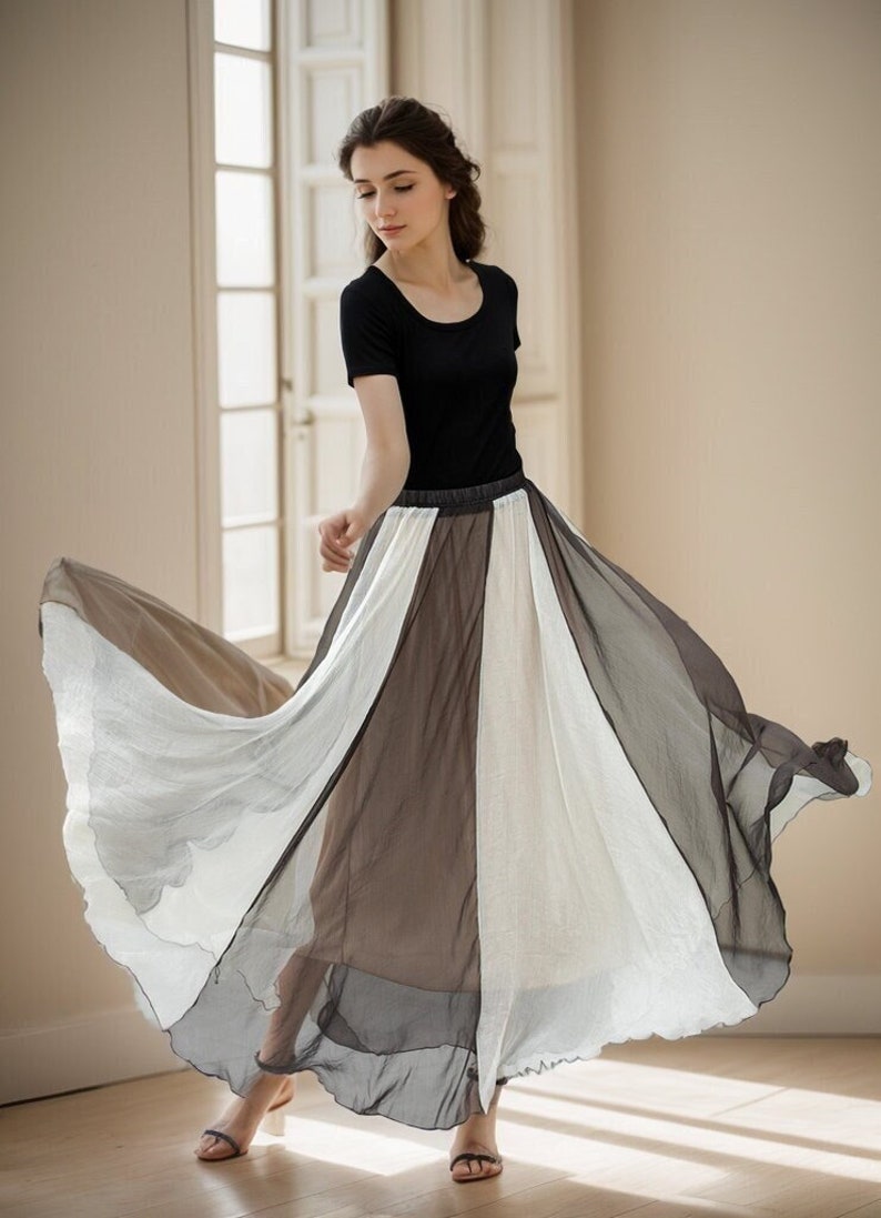 May include: A woman wearing a black top and a long, flowing skirt with alternating panels of white, grey, and brown fabric. The skirt is gathered at the waist and has a flowing, layered design.