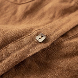 May include: Close-up of a brown linen shirt with a wooden button.