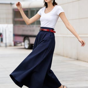 May include: A woman's outfit featuring a white scoop-neck t-shirt, navy blue wide-leg pants, and a red belt. The outfit is accessorized with a black hat, sunglasses, and black sandals with clear heels. The outfit is suitable for casual wear.