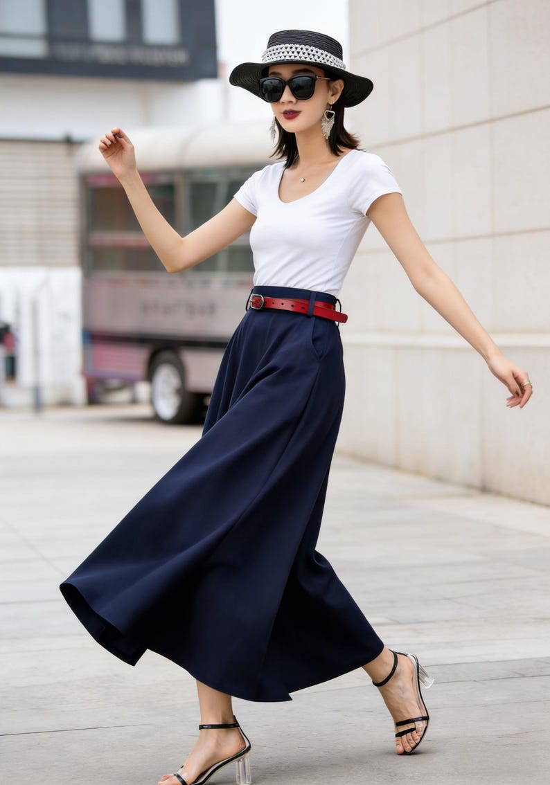 May include: A woman's outfit featuring a white scoop-neck t-shirt, navy blue wide-leg pants, and a red belt. The outfit is accessorized with a black hat, sunglasses, and black sandals with clear heels. The outfit is suitable for casual wear.