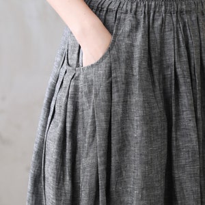 May include: A gray linen skirt with a pleated design and a large pocket on the front. The skirt has a wide waistband and a relaxed fit.