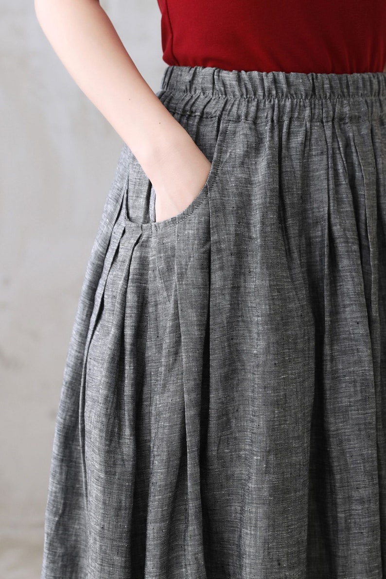 May include: A gray linen skirt with a pleated design and a large pocket on the front. The skirt has a wide waistband and a relaxed fit.