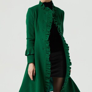 May include: A long, green coat with a ruffled collar and cuffs. The coat has a button-up front and a flared skirt.