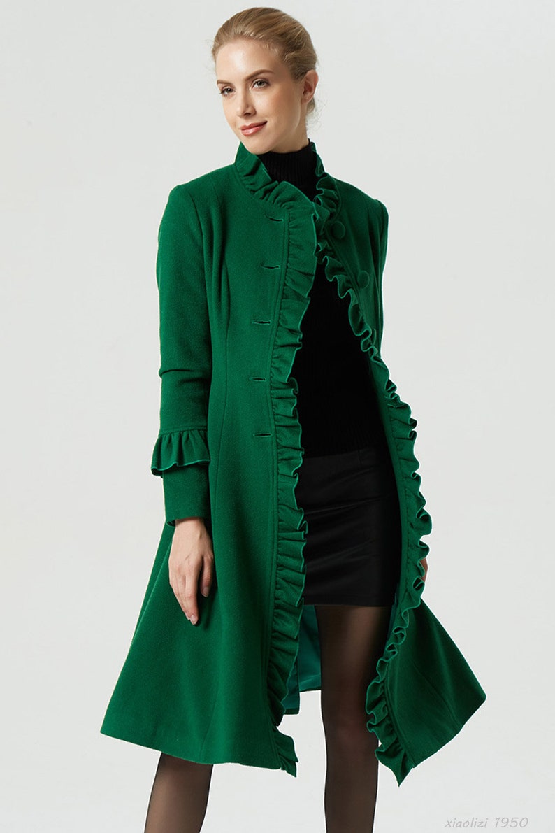May include: A long, green coat with a ruffled collar and cuffs. The coat has a button-up front and a flared skirt.