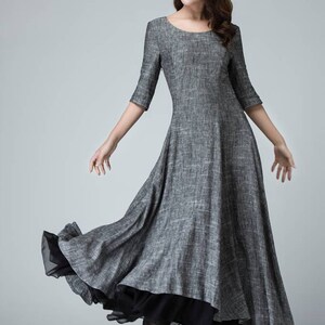 K&ouml;nnte beinhalten: Ein graues Maxikleid mit einem schwarzen Chiffon-Unterrock. Das Kleid hat einen runden Ausschnitt und 3/4 &Auml;rmel. Das Model tr&auml;gt schwarze High Heels.