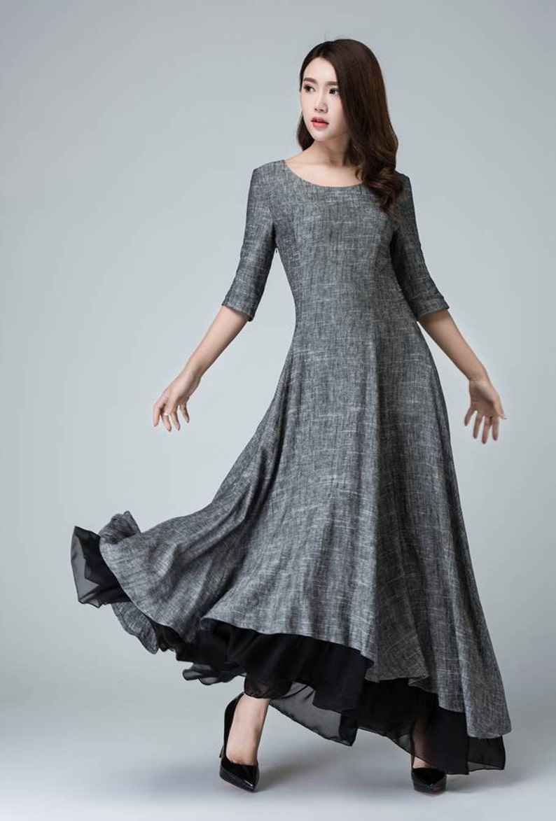 K&ouml;nnte beinhalten: Ein graues Maxikleid mit einem schwarzen Chiffon-Unterrock. Das Kleid hat einen runden Ausschnitt und 3/4 &Auml;rmel. Das Model tr&auml;gt schwarze High Heels.