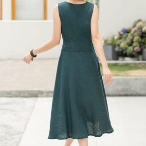 Peut inclure: Une robe midi sans manches de couleur vert fonc&eacute; avec un d&eacute;collet&eacute; en V et un devant boutonn&eacute;. La robe a un corsage ajust&eacute; et une jupe ample.