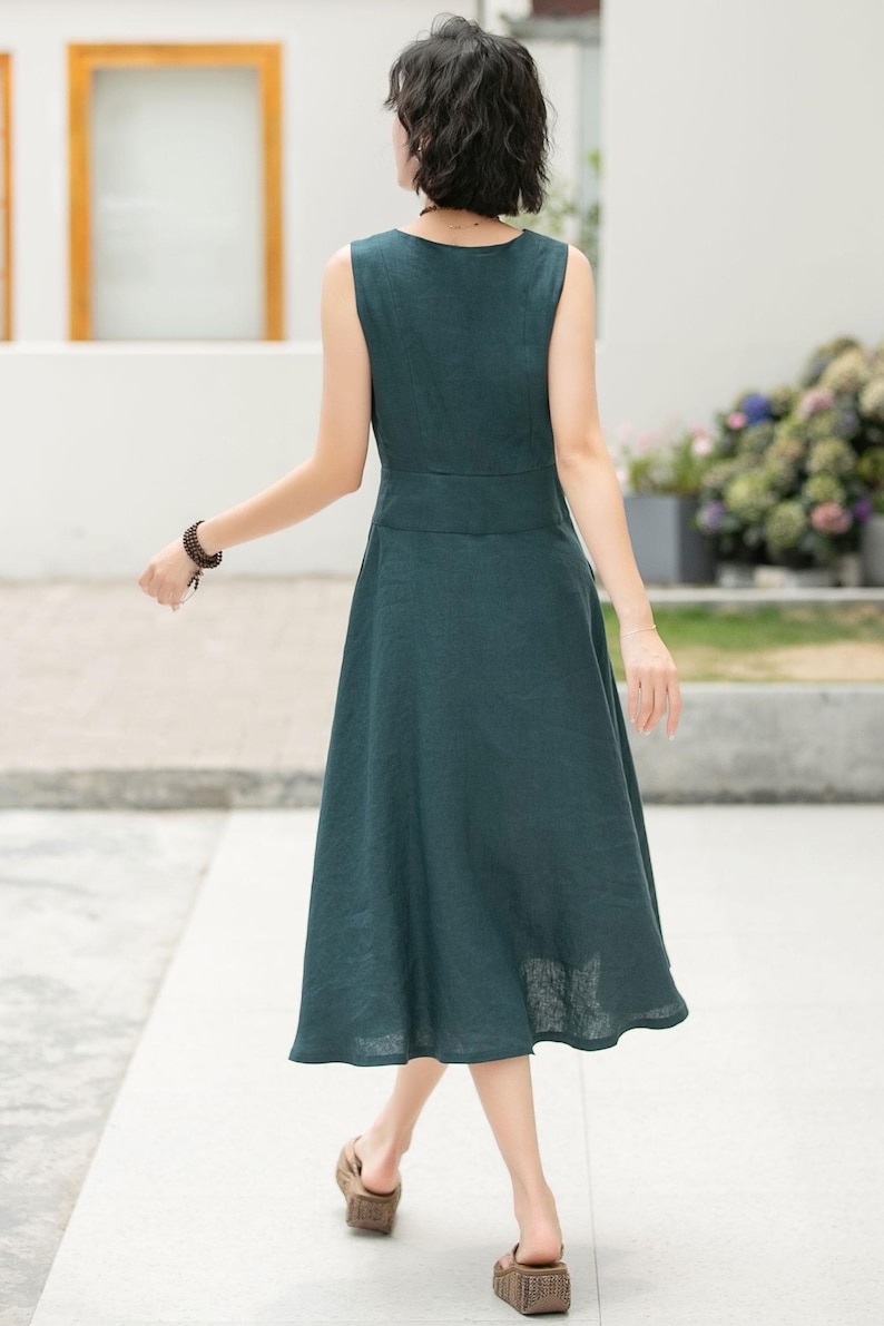 Peut inclure: Une robe midi sans manches de couleur vert fonc&eacute; avec un d&eacute;collet&eacute; en V et un devant boutonn&eacute;. La robe a un corsage ajust&eacute; et une jupe ample.