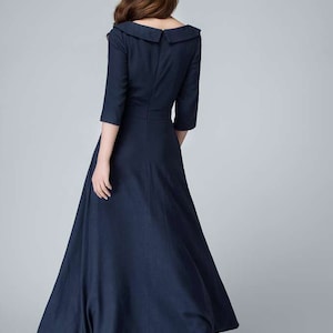May include: A navy blue maxi dress with a wide, sailor-style collar and three-quarter sleeves. The dress has a fitted bodice and a flowing skirt.